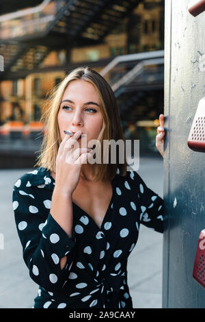 Elegant trendy woman smoking cigar looking away in the city Stock Photo