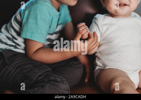 Big brother holding hand of smiling baby sister in polkadot Onesie Stock Photo