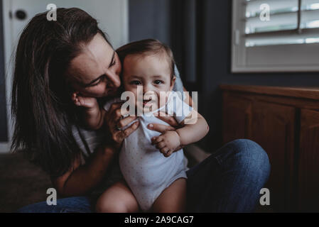 Mid-40â€™s mom snuggles smiling baby on lap Stock Photo