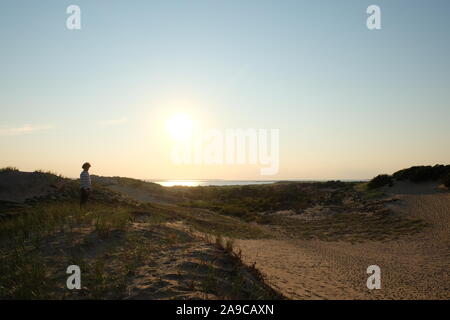 Silhoette of Man Standing in Dunes with Ocean and Sunset in Background Stock Photo