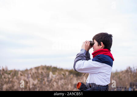 Playful boy looking through binoculars while standing on path Stock Photo