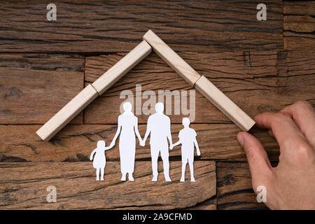 Close-up Of A Person's Hand Making Wooden Dominoes Blocks Roof Over The White Cutout Family Stock Photo