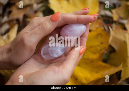 Female hands with orange manicure holding two yoni eggs made from pink quartz and transparent violet amethyst for vumfit, imbuilding or meditation on Stock Photo