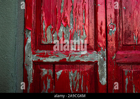 Closeup detailed texture of bright red paint peeling off of an old wooden door. Damp crept in through cracks in the walls. Stock Photo