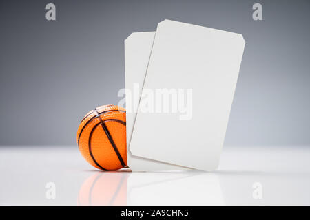 Miniature Basketball With White Blank Tickets On Reflective Desk Against Gray Background Stock Photo