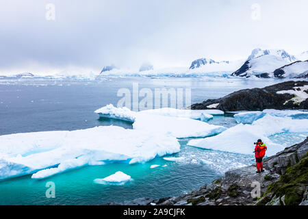 Tourist taking photos of amazing frozen landscape in Antarctica with icebergs, snow, mountains and glaciers, beautiful nature in Antarctic Peninsula w Stock Photo