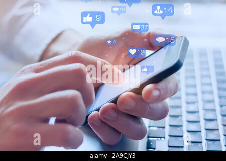 Social media interactions on mobile phone, concept with notification icons of like, message, email, comment and star above smartphone screen, person h Stock Photo