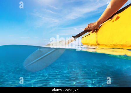 Split view of person kayaking in transparent blue sea, underwater and above water photography of kayak and paddle in warm summer tropical travel desti Stock Photo