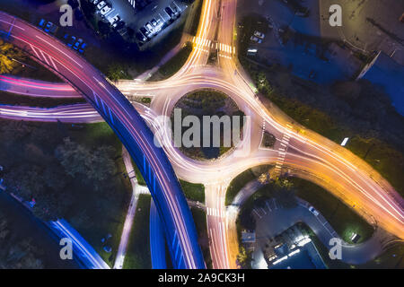 Transportation at night with commuting vehicle traffic creating light trails on the road with motion blur, roundabout and motorway interchange in city Stock Photo