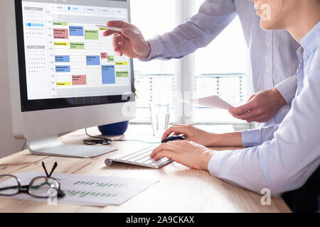 Colleagues planning a meeting with calendar software on computer, search time slot between events, tasks, and appointments, busy business people using Stock Photo