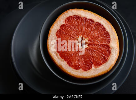 Half of the grapefruit in a gray bowl on a gray plate. Stock Photo
