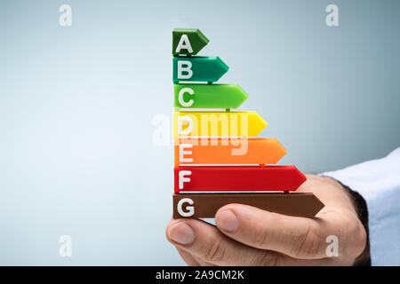 Close-up Of A Man's Hand Holding Plastic Energy Efficiency Graph Against Blue Background Stock Photo