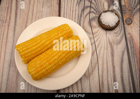 Two ears of boiled corn in a plate and coarse salt on the table. Healthy diet. Fitness diet. For a sweet treat Stock Photo