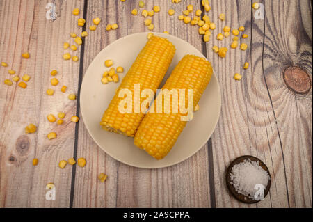 Two ears of boiled corn in a plate, corn kernels and coarse salt on the table. Healthy diet. Fitness diet. For a sweet treat Stock Photo