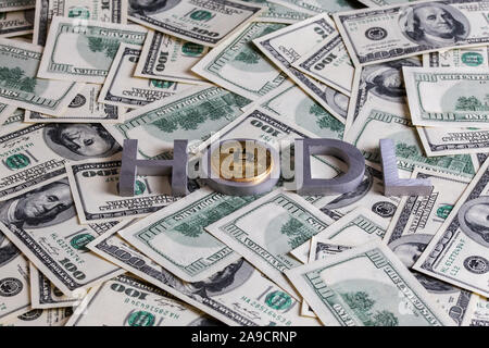 The words HODL laid with aluminium letters and bitcoin shiner on the US dollar banknotes background - with selective focus. Stock Photo