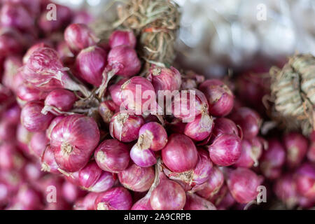 Red onion braid, shallots for sale on a market. Lots of small vendors sell different vegetables on markets in South East Asia, with a huge variety of Stock Photo