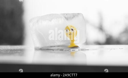 Yellow rubber toy smiley  frozen in an ice cube melting in the sun Stock Photo