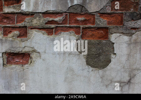 Plaster fallen off a brick wall revealing damaged bricks under it Stock Photo