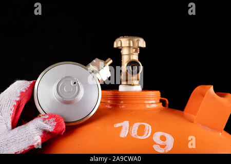 Gas cylinder and propane-butane gas reducer. Accessories for home gas supply. Dark background. Stock Photo