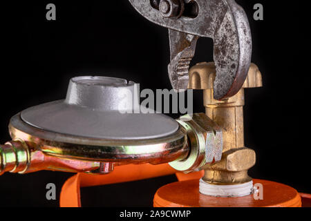 Gas cylinder and propane-butane gas reducer. Installation of a special hose for a metal cylinder. Dark background. Stock Photo