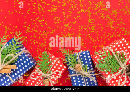 Red and blue gift boxes in polka dots with ribbon and bow and thuja twigs on a red background with glitter gold stars, flat lay, top view Stock Photo