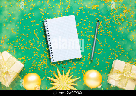 Gold christmas balls and fir twigs and bright shiny christmas garland on a green background with glitter gold stars, open spiral notepad and pen Stock Photo