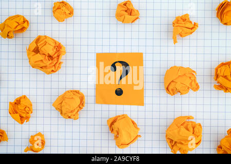 Yellow paper note with question mark on notebook sheet with some yellow crumpled paper balls around it. Close up. Stock Photo
