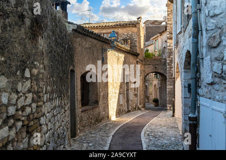 An empty narrow cobblestone street sloping down to a covered archway in the mountaintop medieval village of Saint Paul de Vence, in Southern France Stock Photo