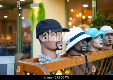 Four mannequin heads of different sexes and race line up outside a store modeling different color hats Stock Photo