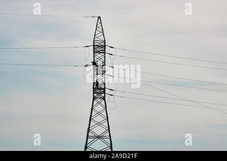 Electricians repairing high voltage power lines against a blue sky. Stock Photo