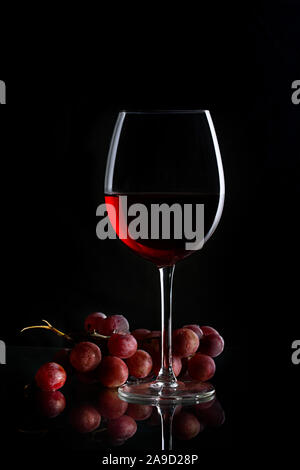 Glass of red wine and bunch of grapes on the dark background Stock Photo