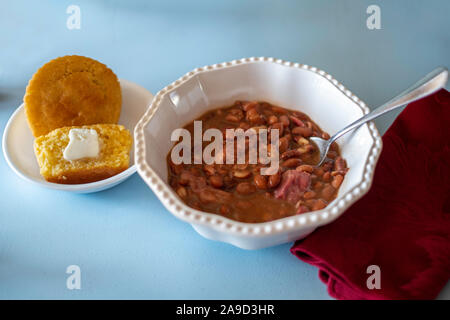 Cooked pinto beans with ham hock and cornbread in a white bowl on a blue painted table. Closeup, USA. Stock Photo