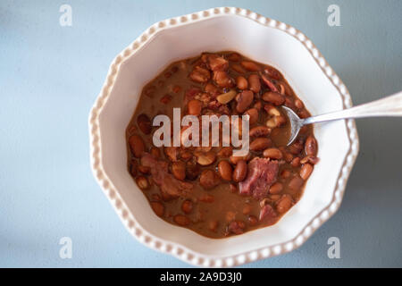 Cooked pinto beans with ham hock in a white bowl, blue background. Shot from above. Stock Photo