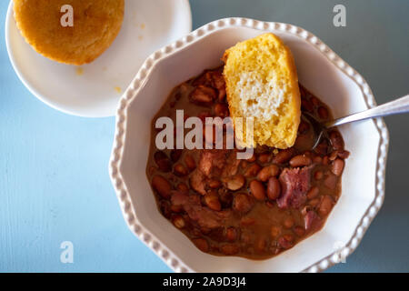 Cooked pinto beans with ham hock and cornbread in a white bowl. Closeup, overhead. Stock Photo
