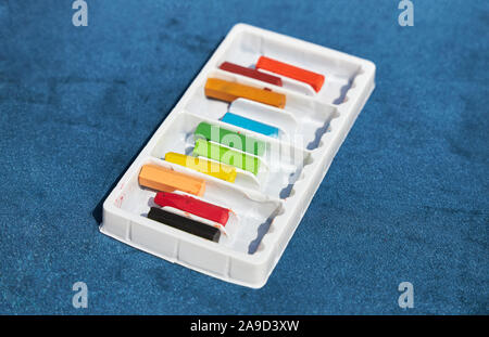 Set of colored crayons in a white box lies on a blue surface. Stock Photo