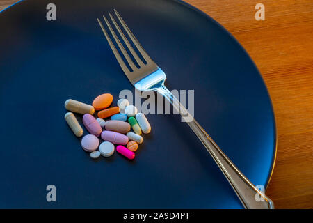 A dark gray plate has an assortment of pills at its center, including prescription medications, over-the-counter drugs, vitamins and other supplements. Stock Photo