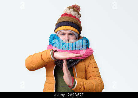 Man in several winter hats and scarfs making time out gesture. I need to stop. Studio shot Stock Photo