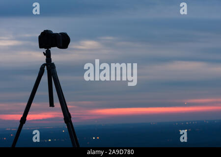 Camera and tripod silhouetted against the sky at sunrise. Stock Photo