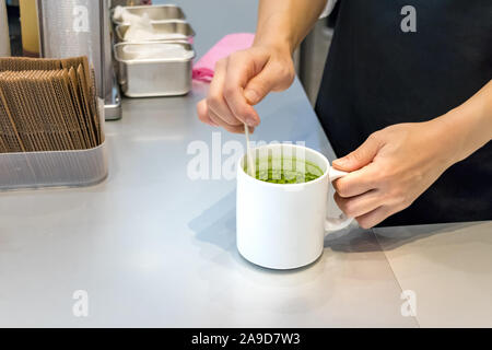 Female barista hands preparing matcha tea on a bowl, mixing it