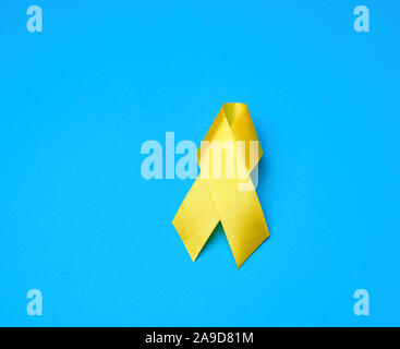 yellow ribbon on a blue background, symbol of the fight against the cat's tumor, problem of suicides and their prevention, close up Stock Photo