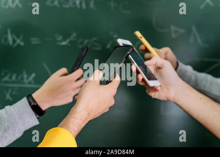 Students using mobile phones in classroom with a chalkboard in the background . Stock Photo