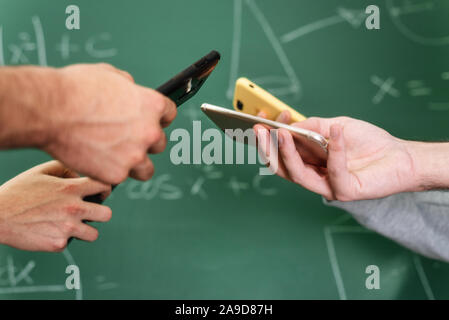 Students using mobile phones in classroom with a chalkboard in the background . Stock Photo