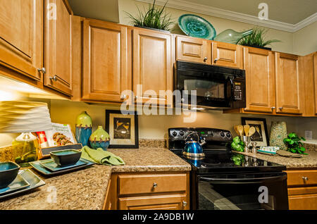 A kitchen features granite countertops, wooden cabinets, a glass cooktop stove, and a microwave at Cypress Cove Apartment Homes in Mobile, Alabama. Stock Photo