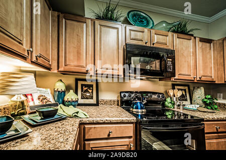 A kitchen features granite countertops, wooden cabinets, a glass cooktop stove, and a microwave at Cypress Cove Apartment Homes in Mobile, Alabama. Stock Photo