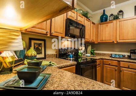 A kitchen features granite countertops, wooden cabinets, a glass cooktop stove, and a microwave at Cypress Cove Apartment Homes in Mobile, Alabama. Stock Photo