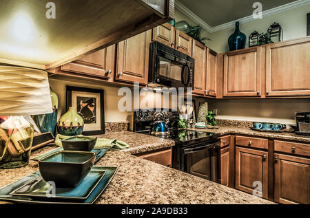 A kitchen features granite countertops, wooden cabinets, a glass cooktop stove, and a microwave at Cypress Cove Apartment Homes in Mobile, Alabama. Stock Photo