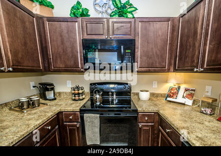 A kitchen features granite countertops, wooden cabinets, a glass cooktop stove, and a microwave at Cypress Cove Apartment Homes in Mobile, Alabama. Stock Photo