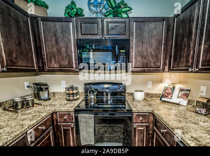 A kitchen features granite countertops, wooden cabinets, a glass cooktop stove, and a microwave at Cypress Cove Apartment Homes in Mobile, Alabama. Stock Photo