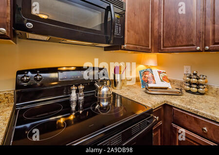 A kitchen features granite countertops, wooden cabinets, a glass cooktop stove, and a microwave at Cypress Cove Apartment Homes in Mobile, Alabama. Stock Photo