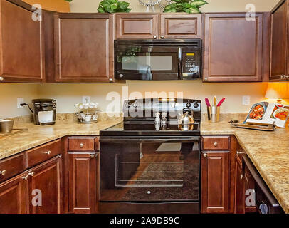 A kitchen features granite countertops, wooden cabinets, a glass cooktop stove, and a microwave at Cypress Cove Apartment Homes in Mobile, Alabama. Stock Photo